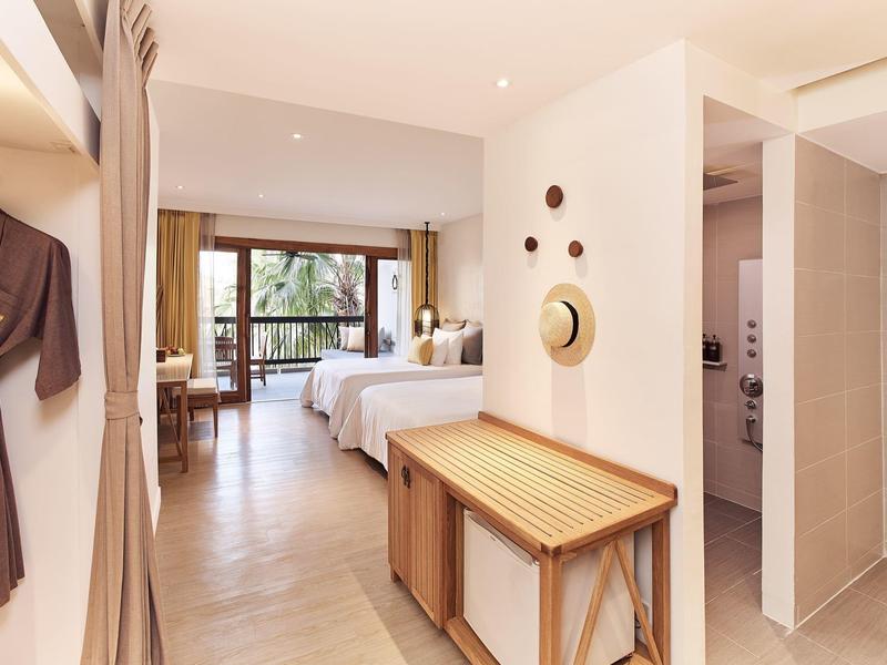 Hell eingerichtetes Hotelzimmer mit Doppelbett, Holzbank und Balkon mit Blick auf Grün.