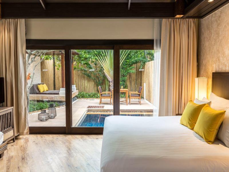 Modernes Hotelzimmer mit großem Bett, Glas-Türen und Blick auf einen Garten mit Pool.