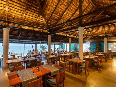 Offenes Restaurant mit Holztischmöbeln, Strohdach und Blick auf das Meer.