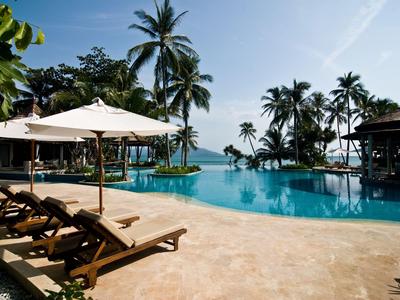 Luxurious pool area with sun loungers and palm trees under blue sky at a tropical vacation spot.