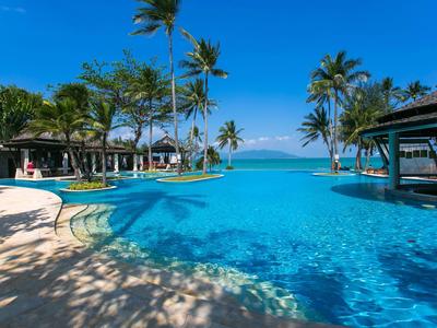 Large pool with blue water, surrounded by palm trees and hammocks under a bright blue sky.