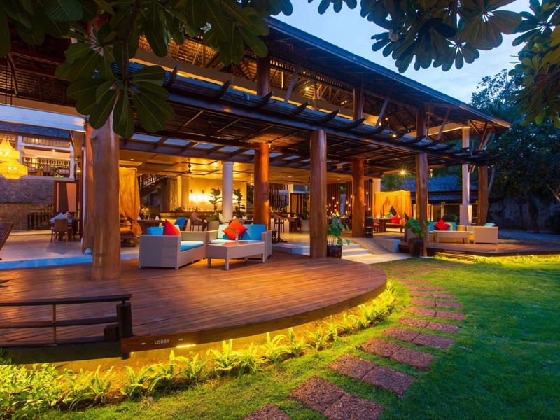 Pohodlná hotelová terasa s teplým osvětlením a zeleným trávníkem za soumraku.