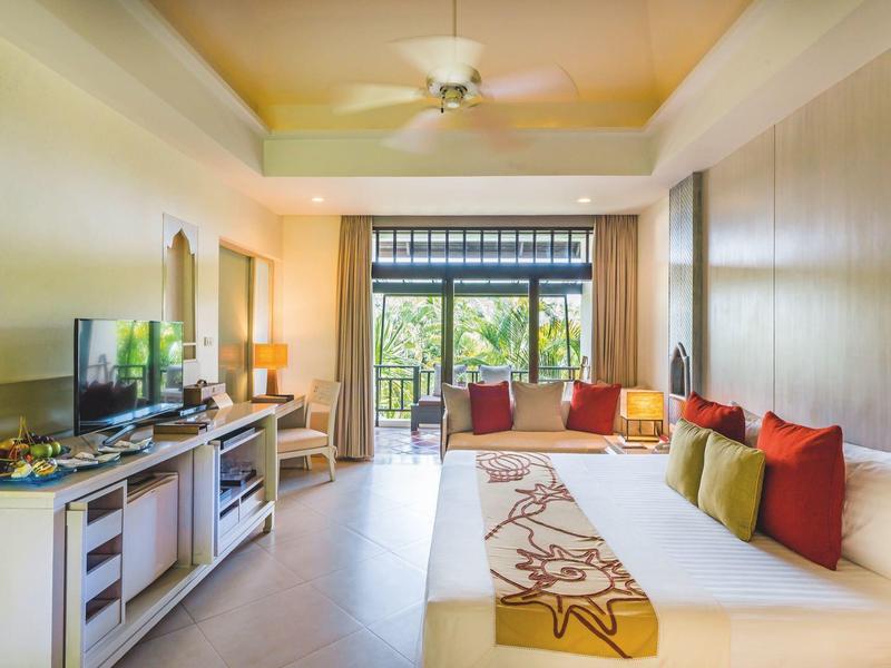 Světý hotelový pokoj se dvěma postelemi, televizí, stropním ventilátorem a balkonem s výhledem na zahradu.