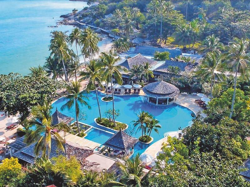Rezort s velkým bazénem obklopeným palmami a mořem v pozadí.