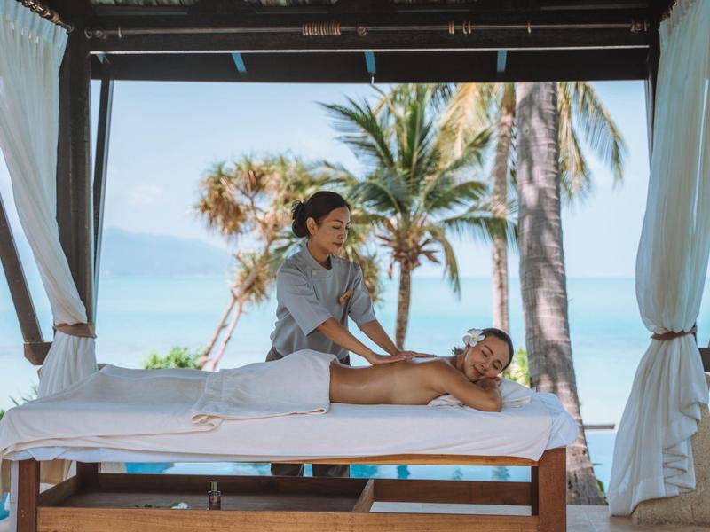 Muž dostává masáž v pavilonu na pláži s palmami a mořem v pozadí.