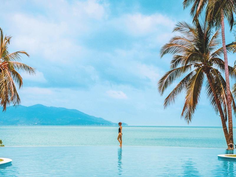 Infinity bazén s výhledem na moře a palmami pod modrou oblohou