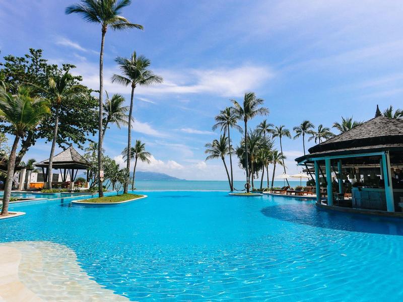 Velký bazén s palmami a barem při tropickém pobřežním resortu