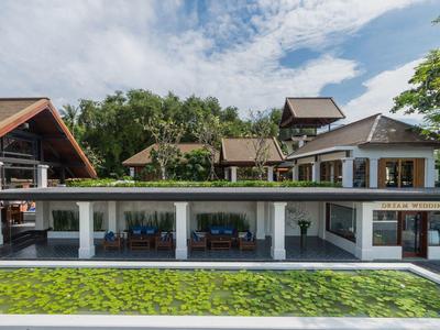 Modernes Haus mit großen Glasfenstern, Gartenteich, Bäumen und blauem Himmel im Hintergrund.