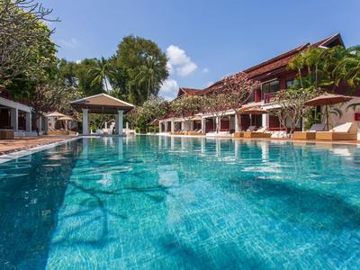 Großer blauer Pool mit Liegen, Palmen und traditionellem roten Gebäude im tropischen Resort.