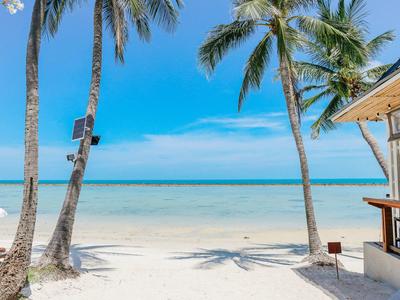 Strand mit weißem Sand, Palmen und einer kleinen Bar am Meer unter blauem Himmel.