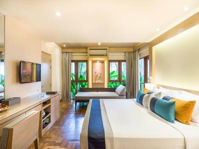 Moderne Hotelzimmer mit großem Bett, hellen Wänden, Holzmöbeln und Panoramafenstern mit Blick aufs Grün.