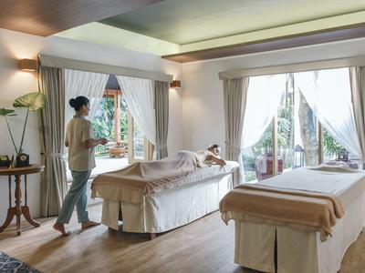 Ein helles Wellness-Zimmer mit zwei Massageliegen, Fensterlicht und pflanzen am Rand.