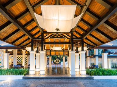 Eingangsbereich mit Holzdecke, weißen Säulen und symmetrischer Beleuchtung bei Nacht.