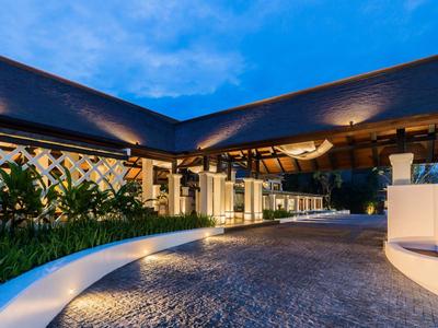 Modernes Gebäude mit schrägem Dach, großer Einfahrt und warmen Lichtern bei Abenddämmerung.