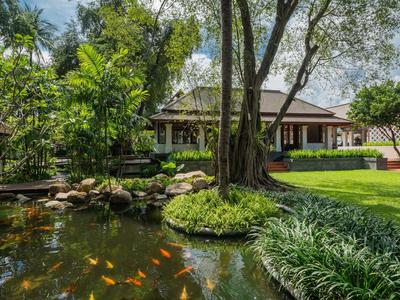 Garten mit großem Teich, bunten Fischen, Bäumen, Rasen und traditionellem Haus im Hintergrund.