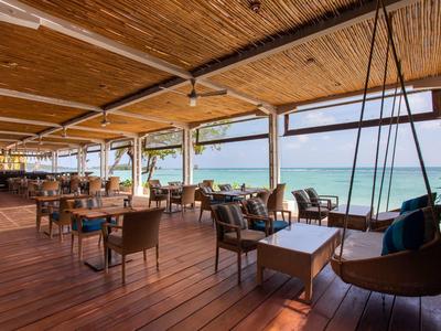 Offenes Strandrestaurant mit Holzboden, Tischen, Stühlen und Schaukelstühlen mit Meeresblick.