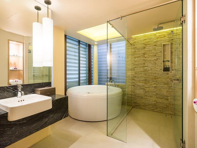 Modernes Badezimmer mit rundem Whirlpool, Glasdusche, Waschbecken und sanfter Beleuchtung.