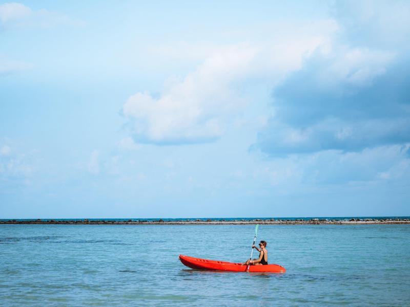 Eine Person paddelt in einem roten Kajak auf ruhigem, blauem Wasser unter bewölktem Himmel.