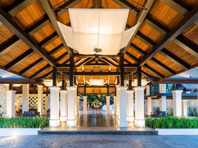 Eingangsbereich mit Holzdecke, weißen Säulen und symmetrischer Beleuchtung bei Nacht.