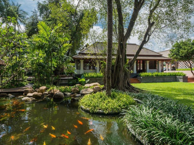 Garten mit großem Teich, bunten Fischen, Bäumen, Rasen und traditionellem Haus im Hintergrund.