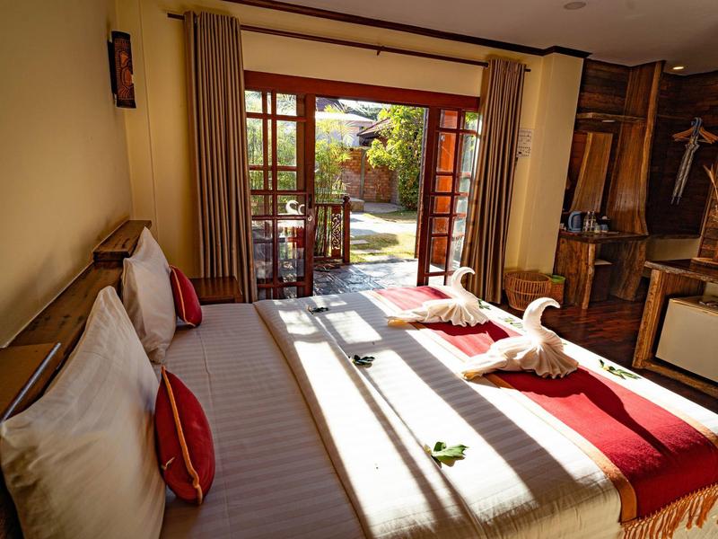 Gemütliches Schlafzimmer mit großem Bett, roten Akzenten und Blick auf sonnigen Garten.