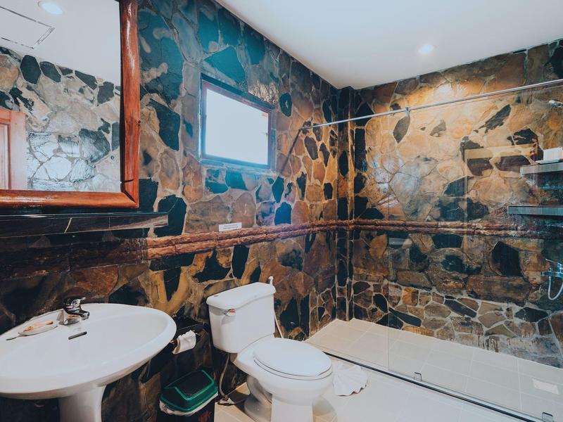 Badezimmer mit rustikalen Steinwänden, Waschbecken, Toilette, Dusche und kleinem Fenster.