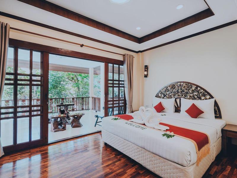 Schlafzimmer mit offenem Balkon, Holzboden, Doppeltbett und braunen Vorhängen.