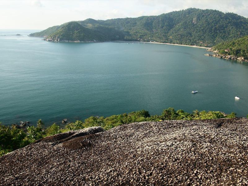 Blick auf eine Bucht mit ruhigem Wasser und bewaldeten Hügeln im Hintergrund bei klarem Himmel.