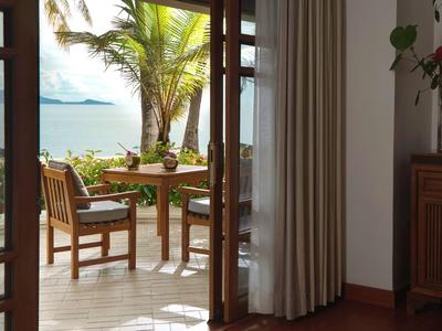 Taras z drewnianym stołem i krzesłami, widok na palmy i morze w świetle słonecznym