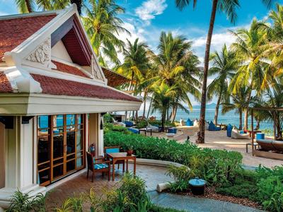 Tropisches Resort mit Holzhaus, Palmen, blauer Himmel und Meer im Hintergrund.