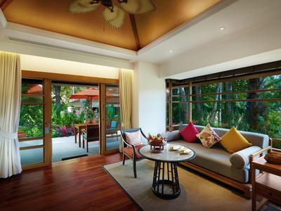 Salon hotelowy z sofą, stołem i widokiem na bujną zieleń na zewnątrz.