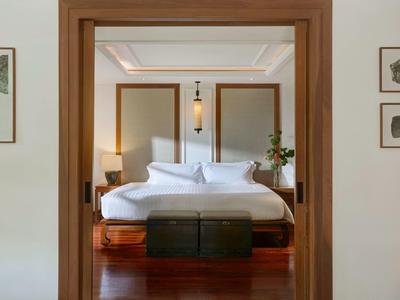 Widok przez framugę drzwi na elegancki pokój hotelowy z łóżkiem podwójnym i drewnianą podłogą.