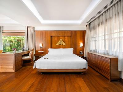 Jasny pokój hotelowy z dużym łóżkiem, drewnianą podłogą i biurkiem przy oknie.