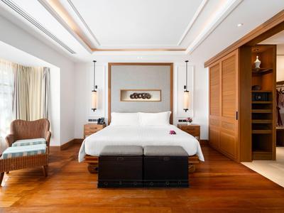 Nowoczesny pokój hotelowy z dużym łóżkiem, drewnianą podłogą i przytulnym miejscem do siedzenia przy oknie.