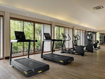 Nowoczesna siłownia z bieżniami i dużymi oknami z widokiem na zieleń.