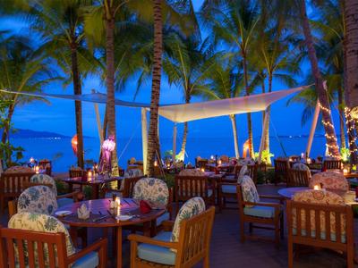 Wieczorna restauracja na świeżym powietrzu z kolorowym oświetleniem i widokiem na morze między palmami.