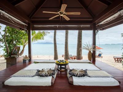 Otwarty pawilon z materacami na drewnianej podłodze z widokiem na piaszczystą plażę i morze.