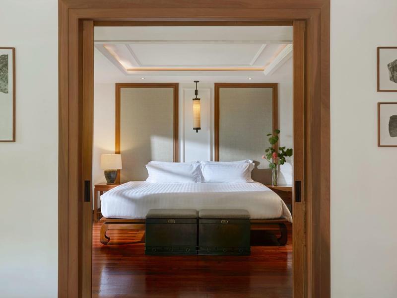 Widok przez framugę drzwi na elegancki pokój hotelowy z łóżkiem podwójnym i drewnianą podłogą.