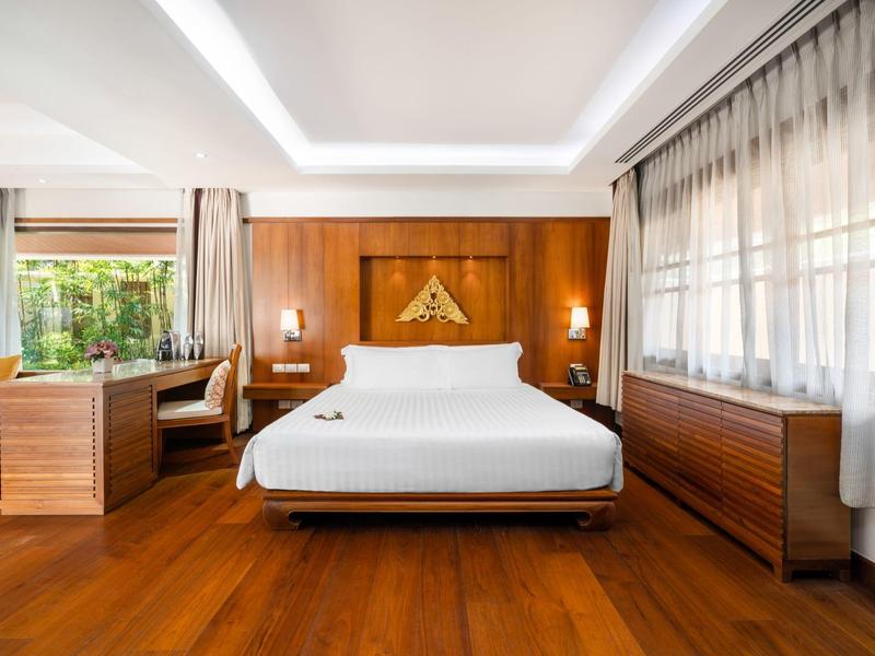 Jasny pokój hotelowy z dużym łóżkiem, drewnianą podłogą i biurkiem przy oknie.