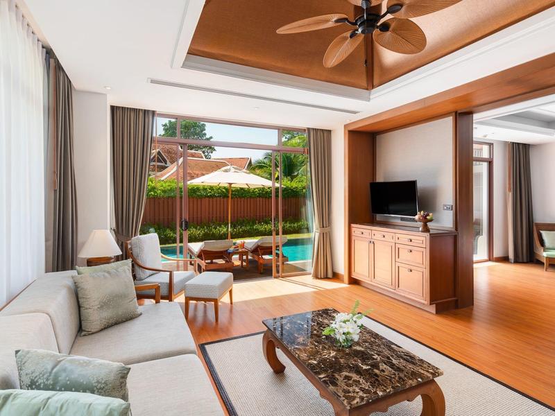 Jasny pokój hotelowy z przytulnym salonem, wentylatorem sufitowym i dostępem do tarasu z widokiem na ogród.