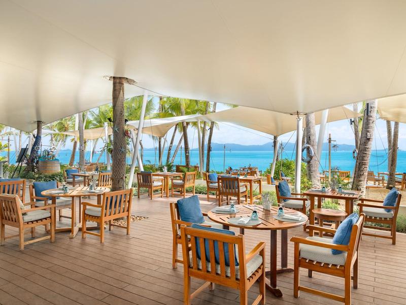 Otwarta część restauracyjna z drewnianymi meblami i widokiem na morze w słoneczny dzień.