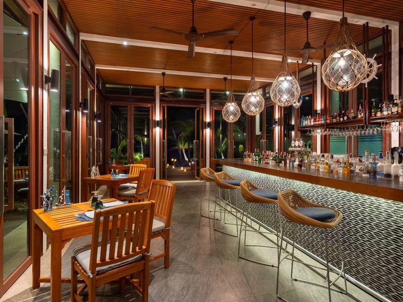 Elegancki bar hotelowy z hokerami i przytulnymi drewnianymi stołami w ciepło oświetlonym pomieszczeniu.