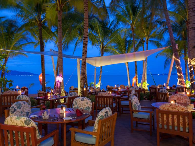 Wieczorna restauracja na świeżym powietrzu z kolorowym oświetleniem i widokiem na morze między palmami.