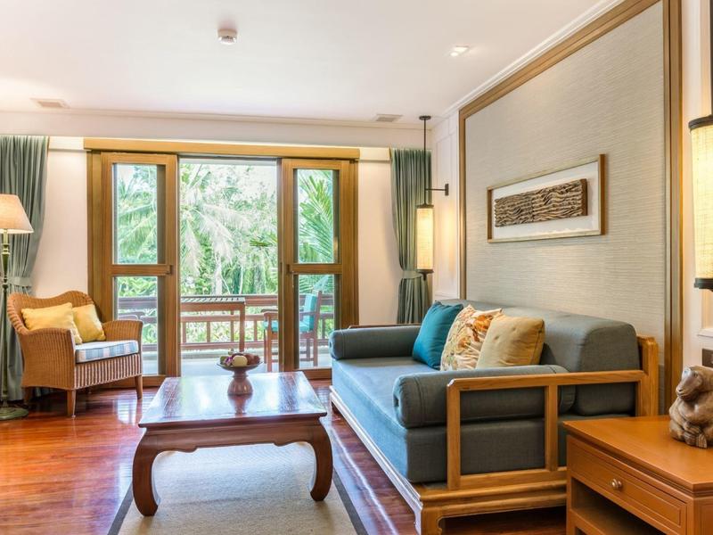 Jasny salon z dużymi oknami, sofą, drewnianymi meblami i widokiem na naturę.