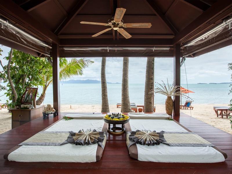 Otwarty pawilon z materacami na drewnianej podłodze z widokiem na piaszczystą plażę i morze.