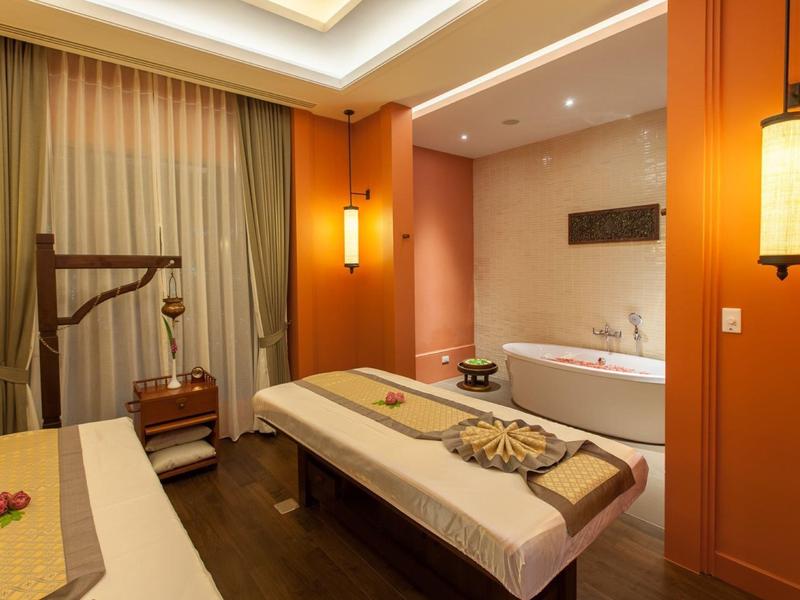 Jasny pokój spa z dwoma stołami do masażu i wanną w ciepłych pomarańczowych tonach.