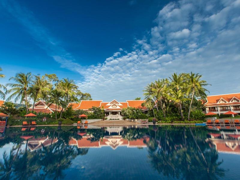 Ośrodek z czerwonymi dachami, palmami i dużym basenem pod niebieskim niebem z chmurami
