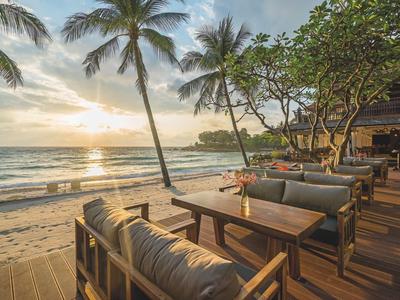 Gemütliche Sitzplätze mit Holzmöbeln am Strand, Palmen und Sonnenuntergang am Meer.
