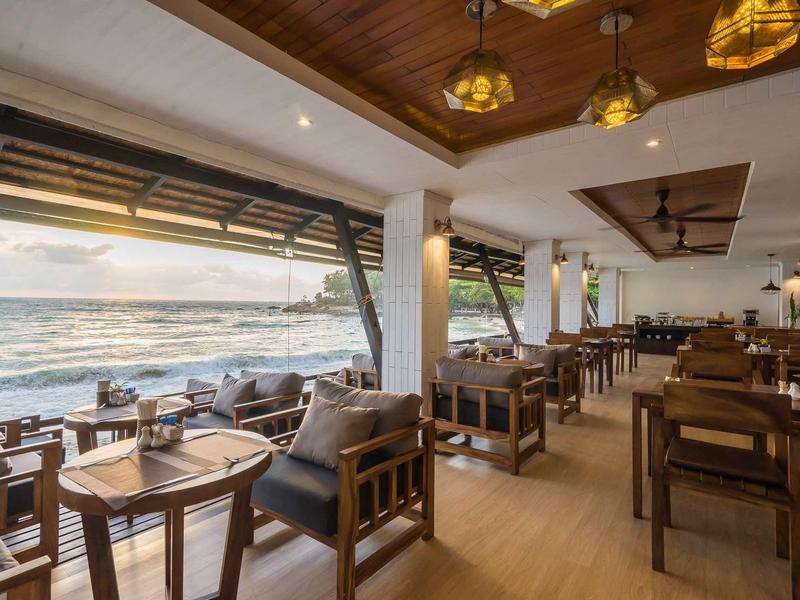 Open restaurant with wooden furniture and sea view at sunset.