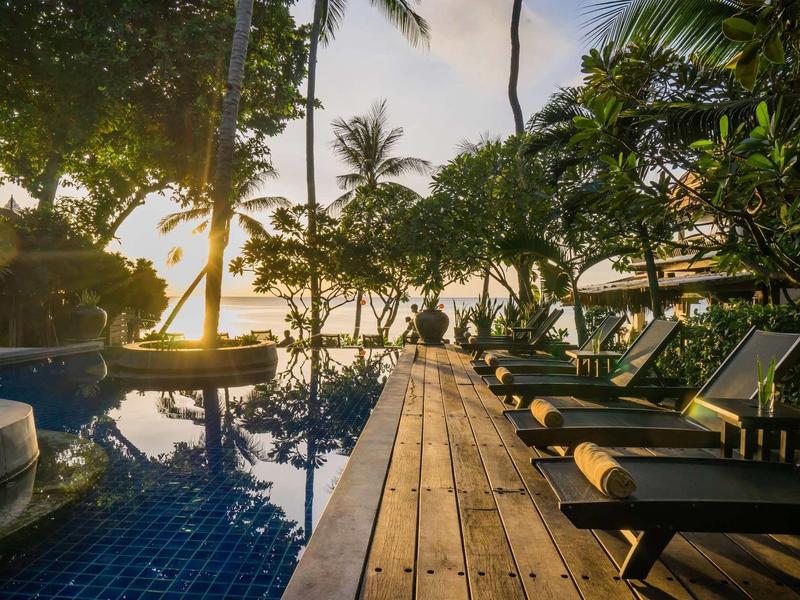 Sunset by the pool with lounge chairs and tropical trees in a hotel resort.